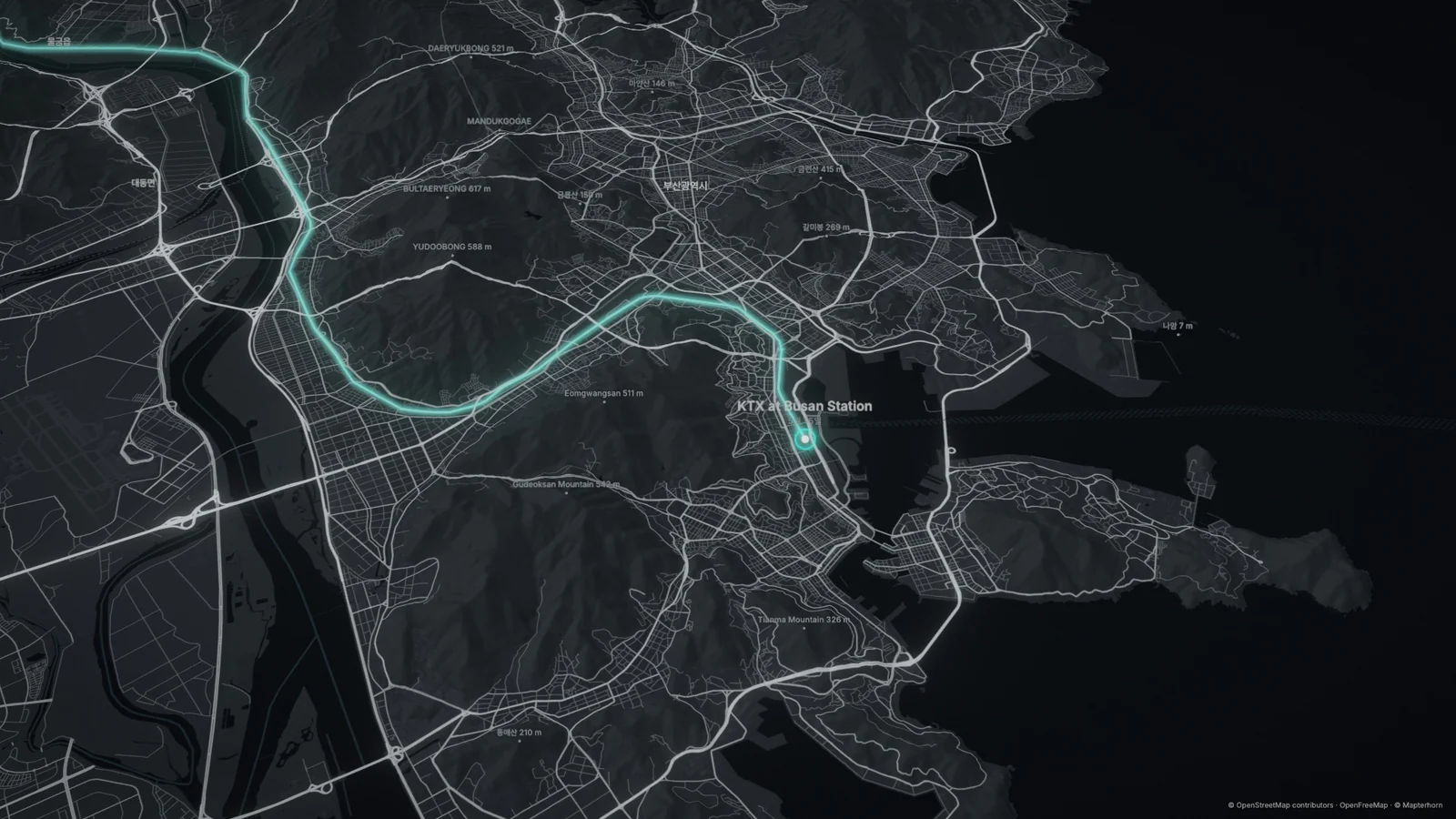 Film frame: the KTX line traced along the railway into Busan Station, over shaded hills with peak names.